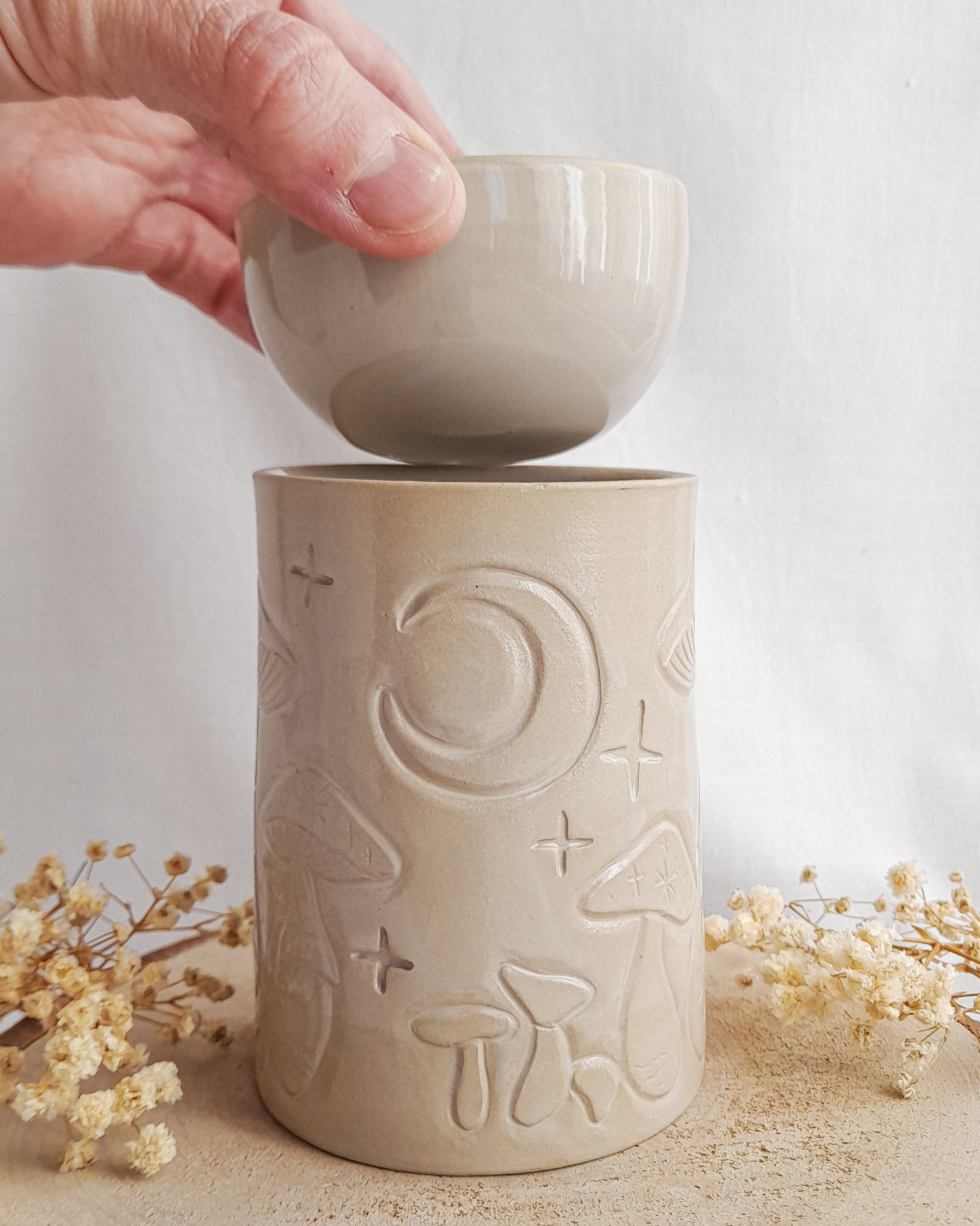 Ceramiczny kominek do podgrzewania olejków i wosków ze zdejmowaną miseczką. Kominek w kolorze beżowym z rzeźbionymi muchomorkami, księżycem i gwiazdami.