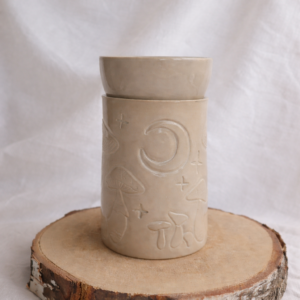 Ceramiczny kominek w kolorze beżowym, z unikatowym rzeźbieniem przedstawiającym muchomorki, księżyc i gwiazdy